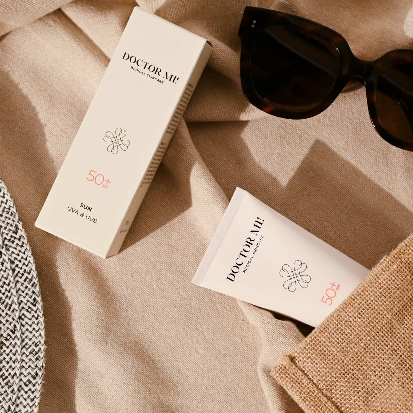 DOCTOR MI! PROTECTING CREAM SPF50 Sonnenschutz mit Lichtschutzfaktor 50+ und Vitamin E für maximalen Schutz in weißer Tube neben weißer Verpackung auf beiger Stranddecke